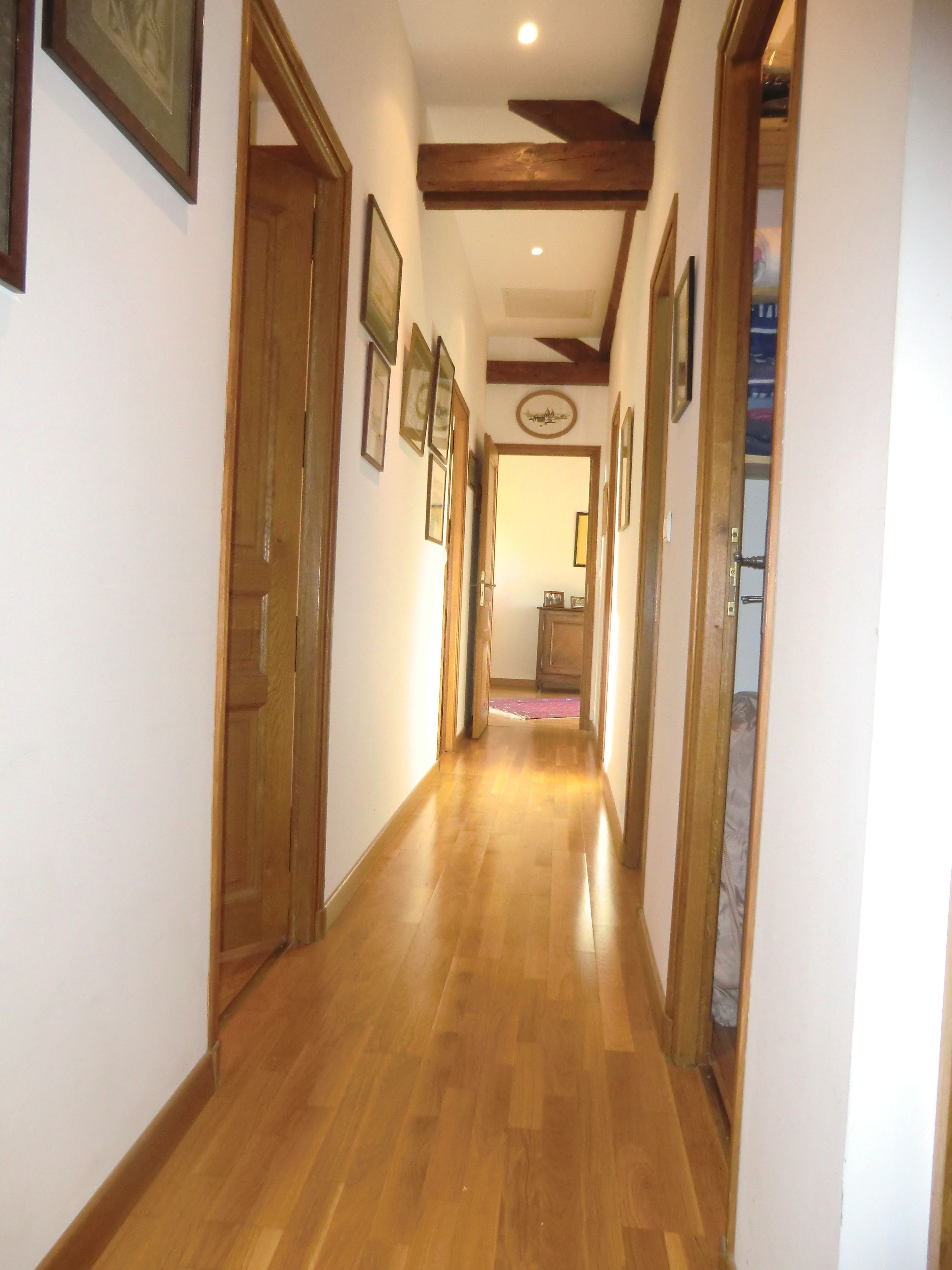 Un pasillo con piso de madera, puertas de madera y cuadros en las paredes.