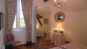 Een slaapkamer met een bed, een stoel, een spiegel, een kroonluchter en een raam met gordijnen.