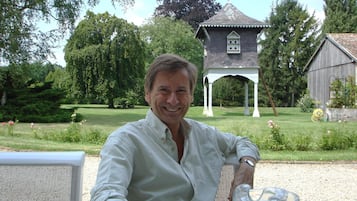 A man seated at an outdoor table with a clear view of a gazebo and a barn in the background.