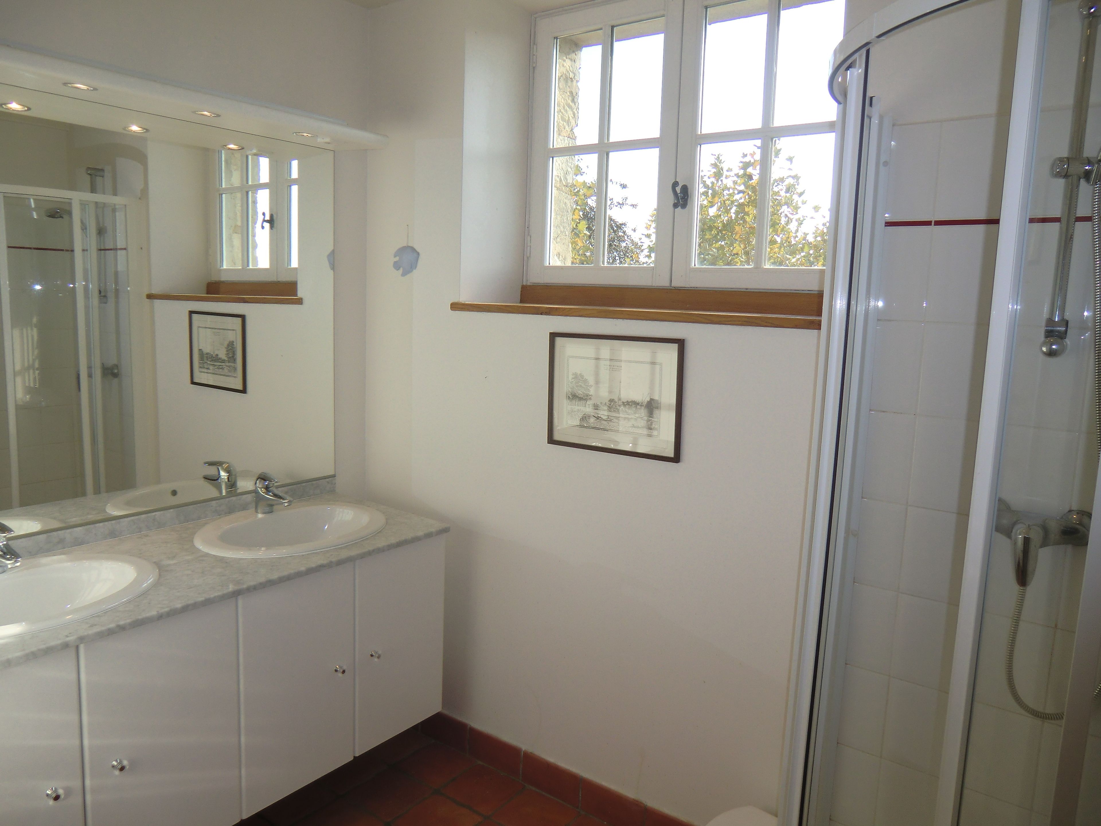 Une salle de bain avec deux lavabos, une douche et des tableaux encadrés au mur.