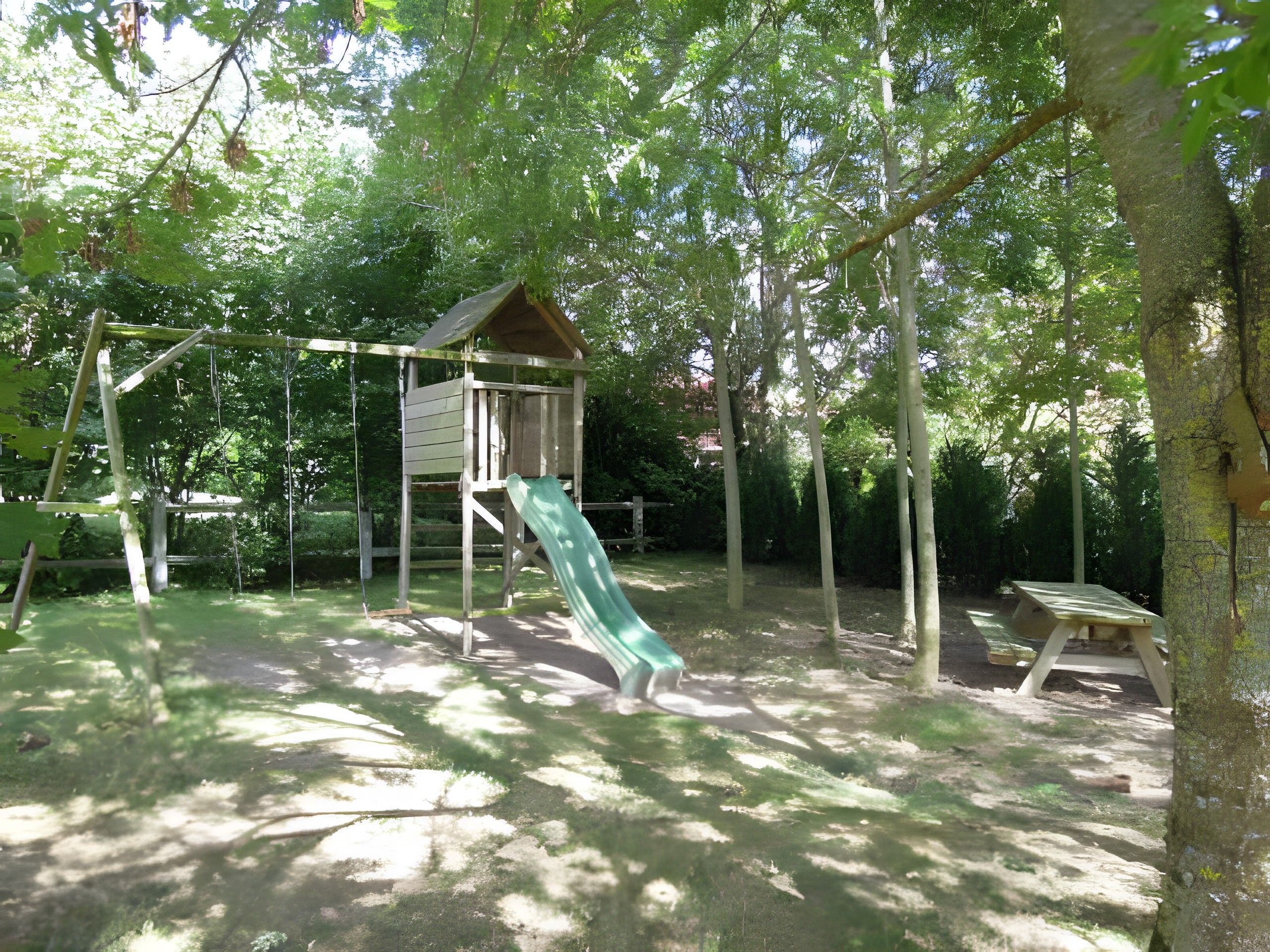 Une aire de jeux avec un toboggan et des balançoires, entourée d’arbres.