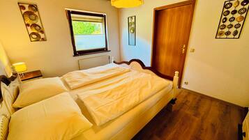 Une chambre à coucher avec un lit double, une fenêtre, un radiateur, une porte en bois et un luminaire fixé au mur.