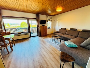 A cozy living room with a sofa, a dining table with chairs, a TV, and a view of the outdoors.