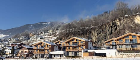 Schneebedeckte Landschaft mit Holzbauten, klarem Himmel und einem Bergpanorama im Hintergrund.