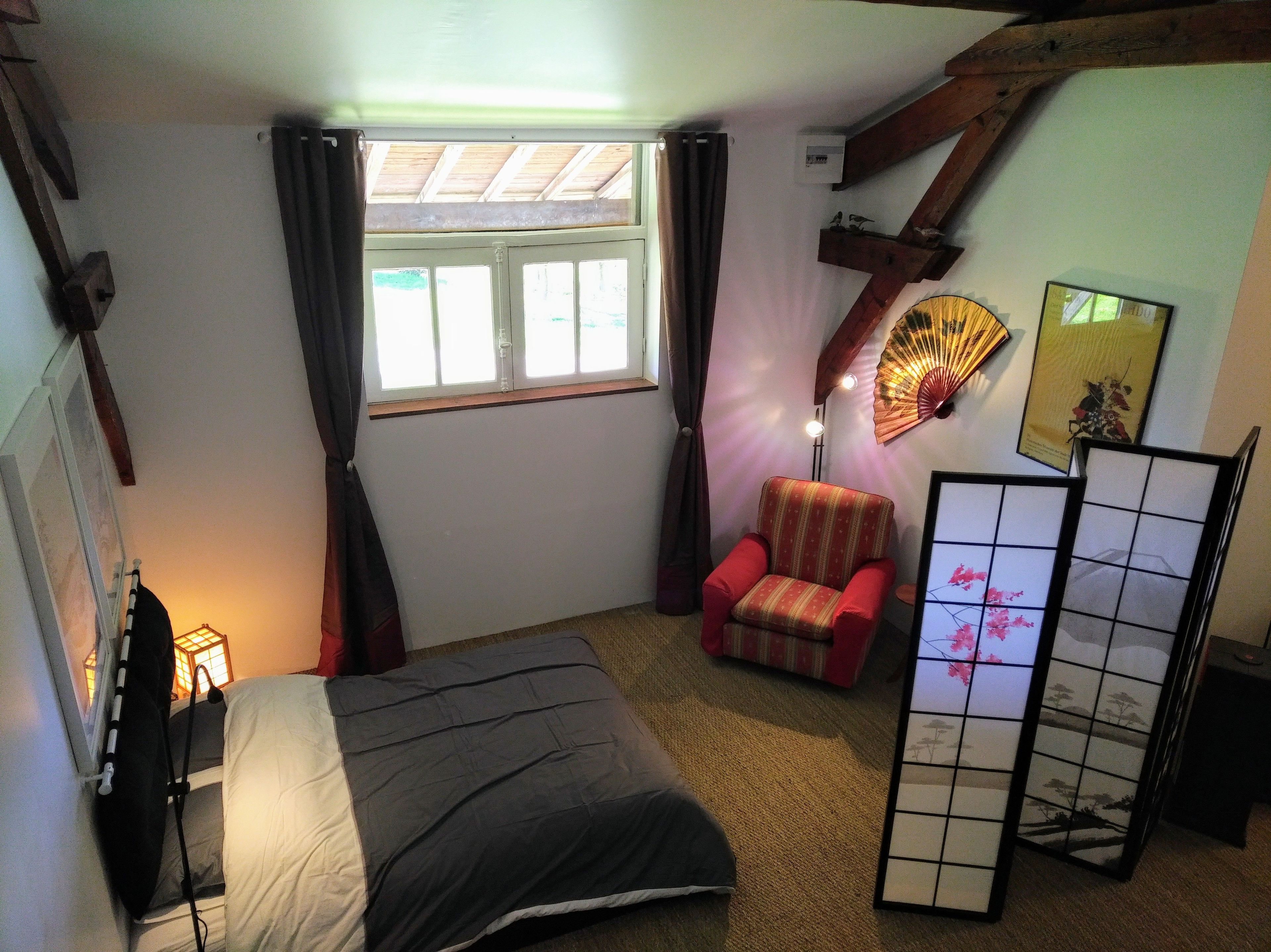 A bedroom with a bed, a chair, a fan, and a traditional screen.