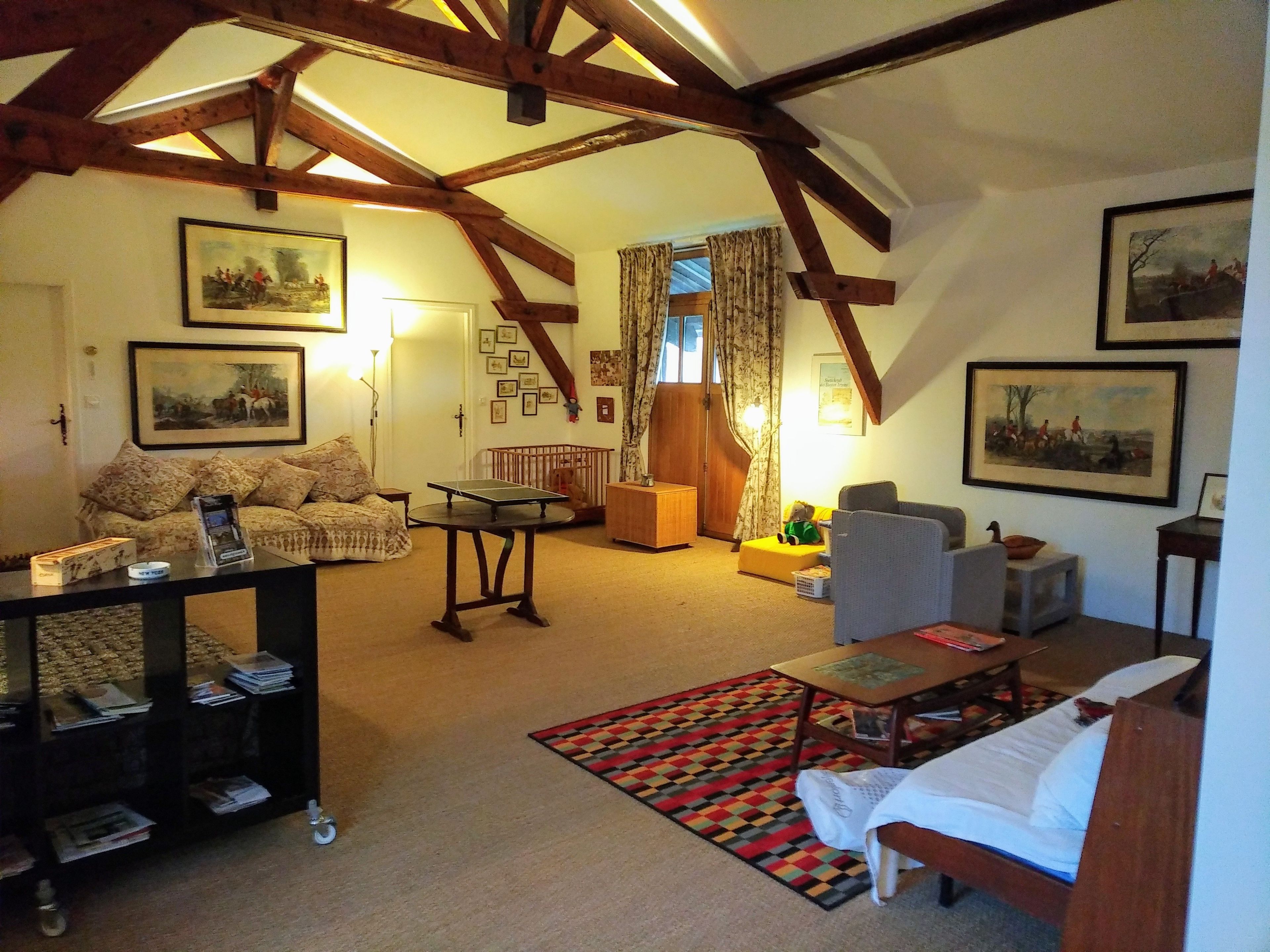 A cozy living room with a high ceiling, wooden beams, a sofa, a coffee table, a patterned rug, and framed artwork on the walls.
