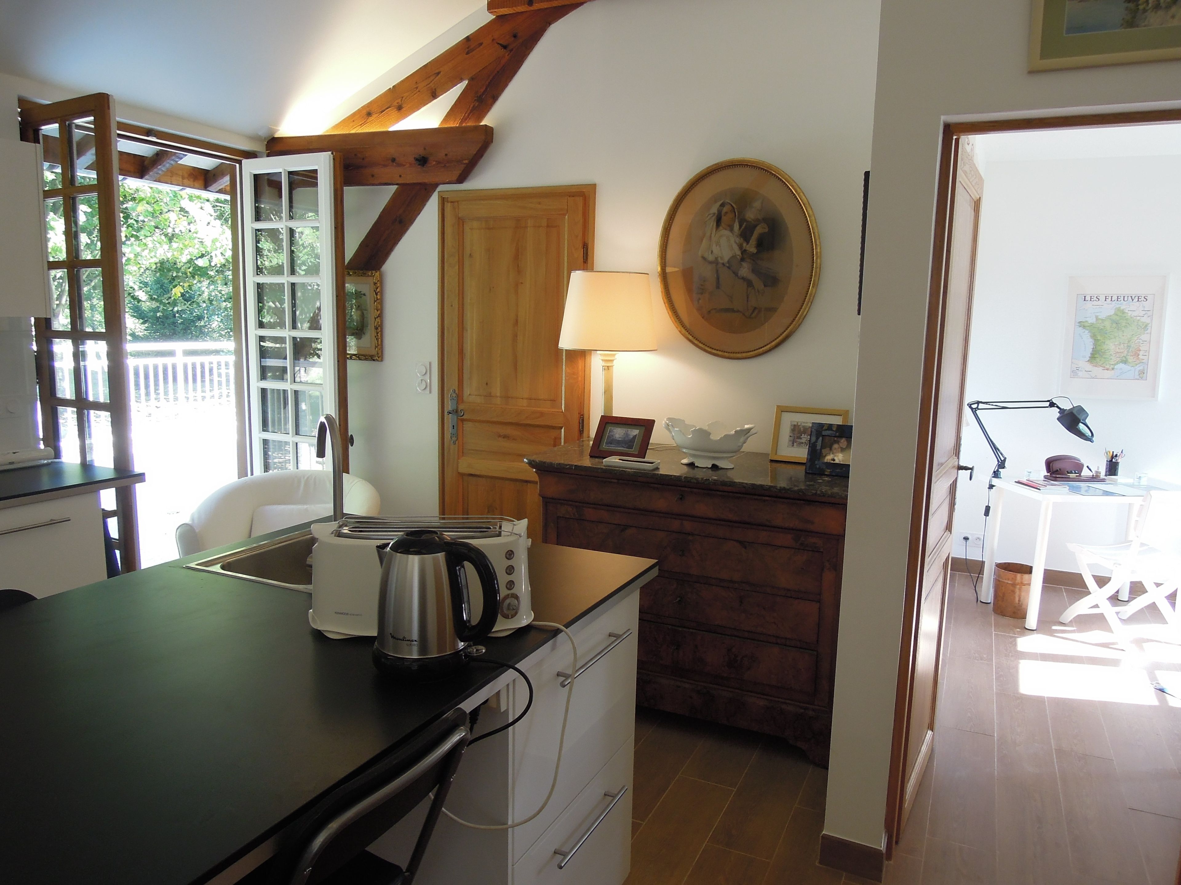 Cocina con tostadora, hervidor y un armario de madera. Hay una mesa de comedor con sillas y una lámpara.