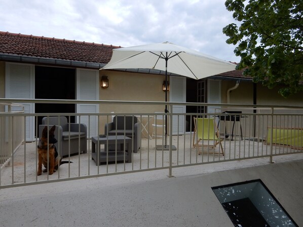 A covered outdoor seating area with chairs and a table, a dog, and a white fence.