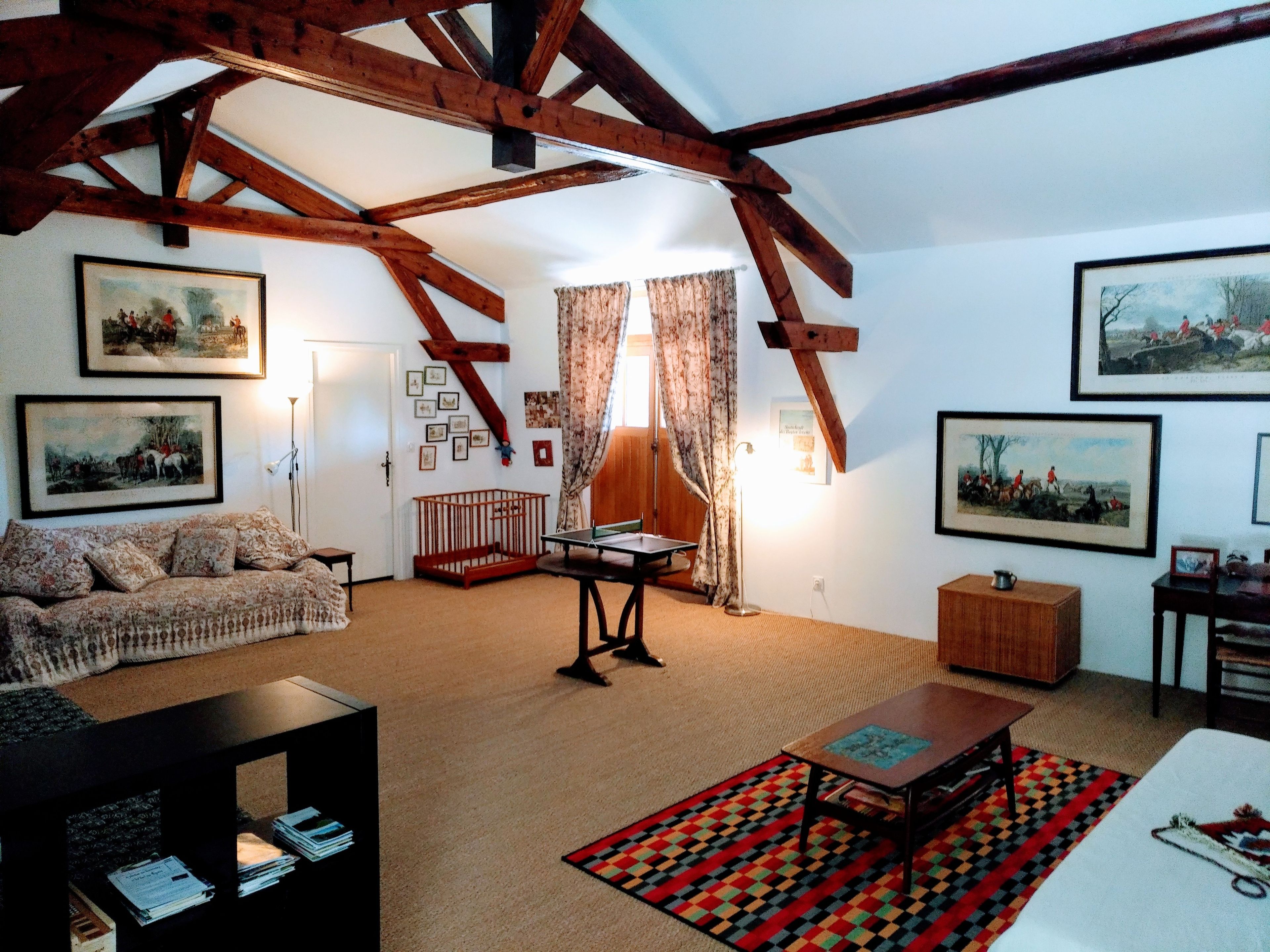 A living room with a high ceiling, wooden beams, a sofa, a coffee table, a rug, and framed pictures on the walls.