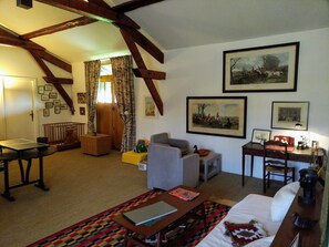 A cozy living room with a high ceiling, wooden beams, a comfortable sofa, a small table, and a bed.