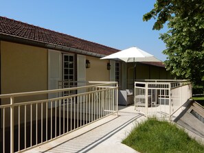 A building with a tiled roof, a balcony with a white railing, and a covered seating area with a white umbrella.