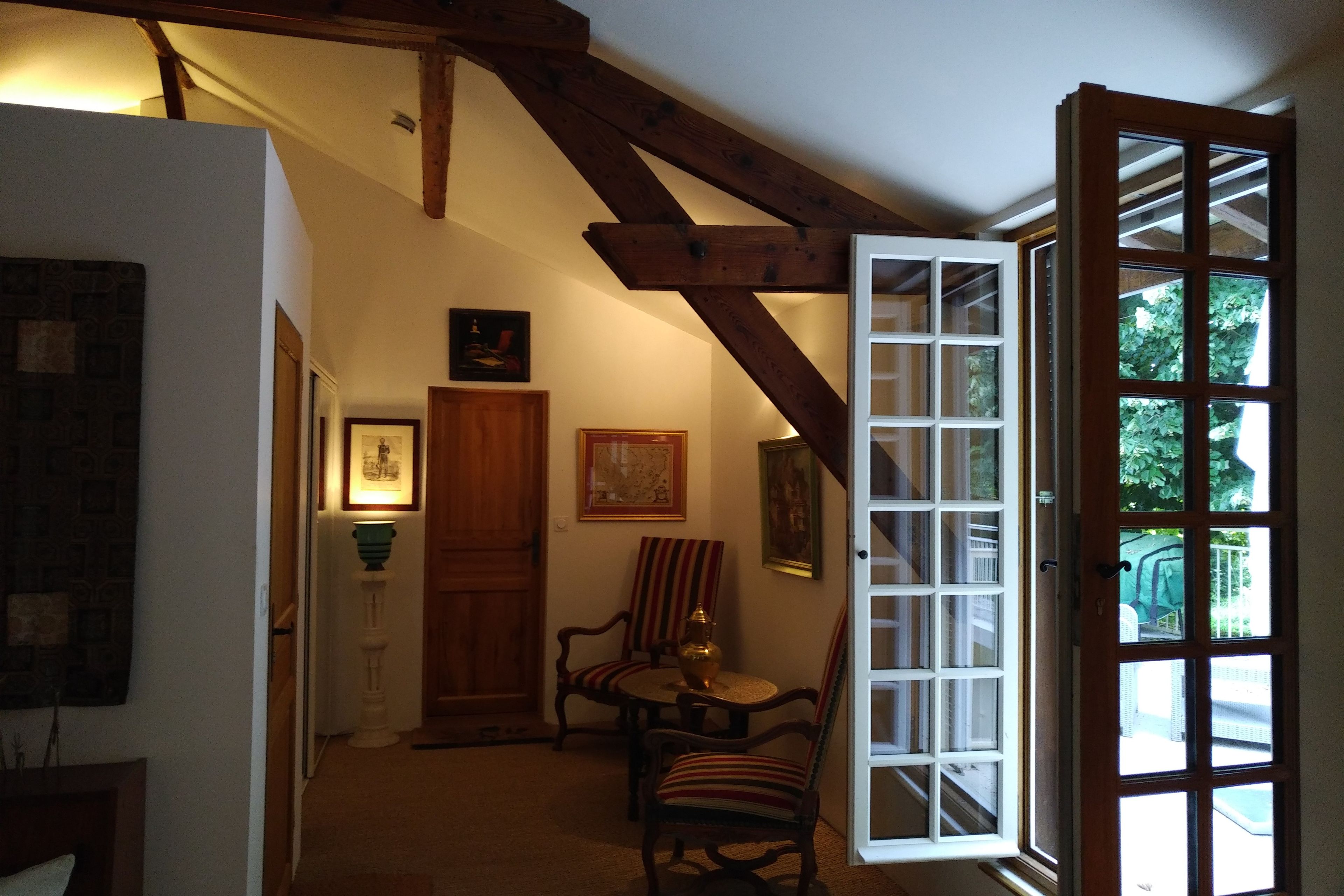 A room with a wooden ceiling, a door, a chair, a table, and a window with multiple panes.