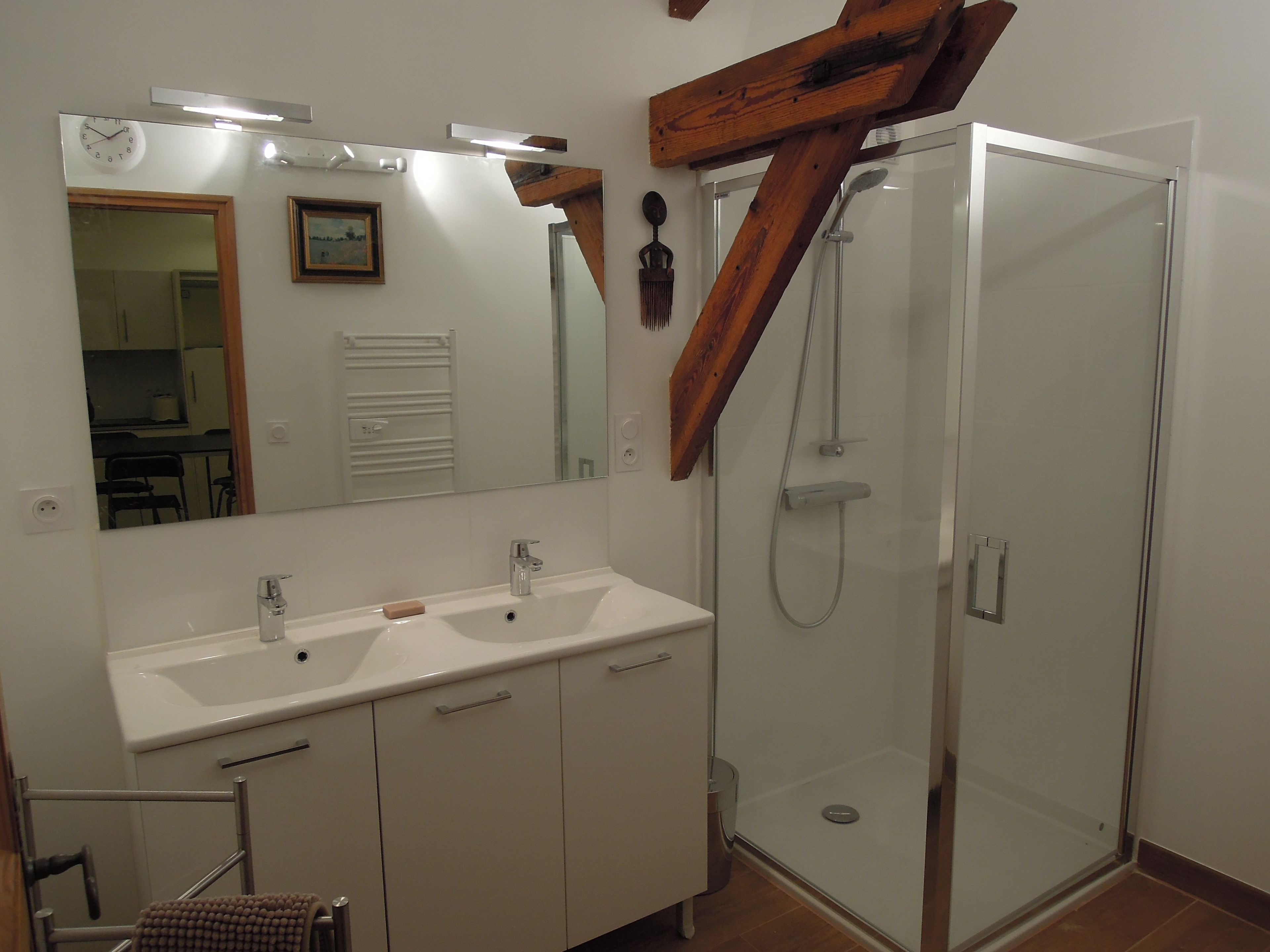 Un baño con tocador doble lavamanos, un espejo grande, cabina de ducha de vidrio y vigas de madera.