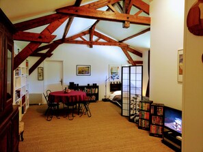 A cozy attic room with a dining table, bookshelves, and a television.