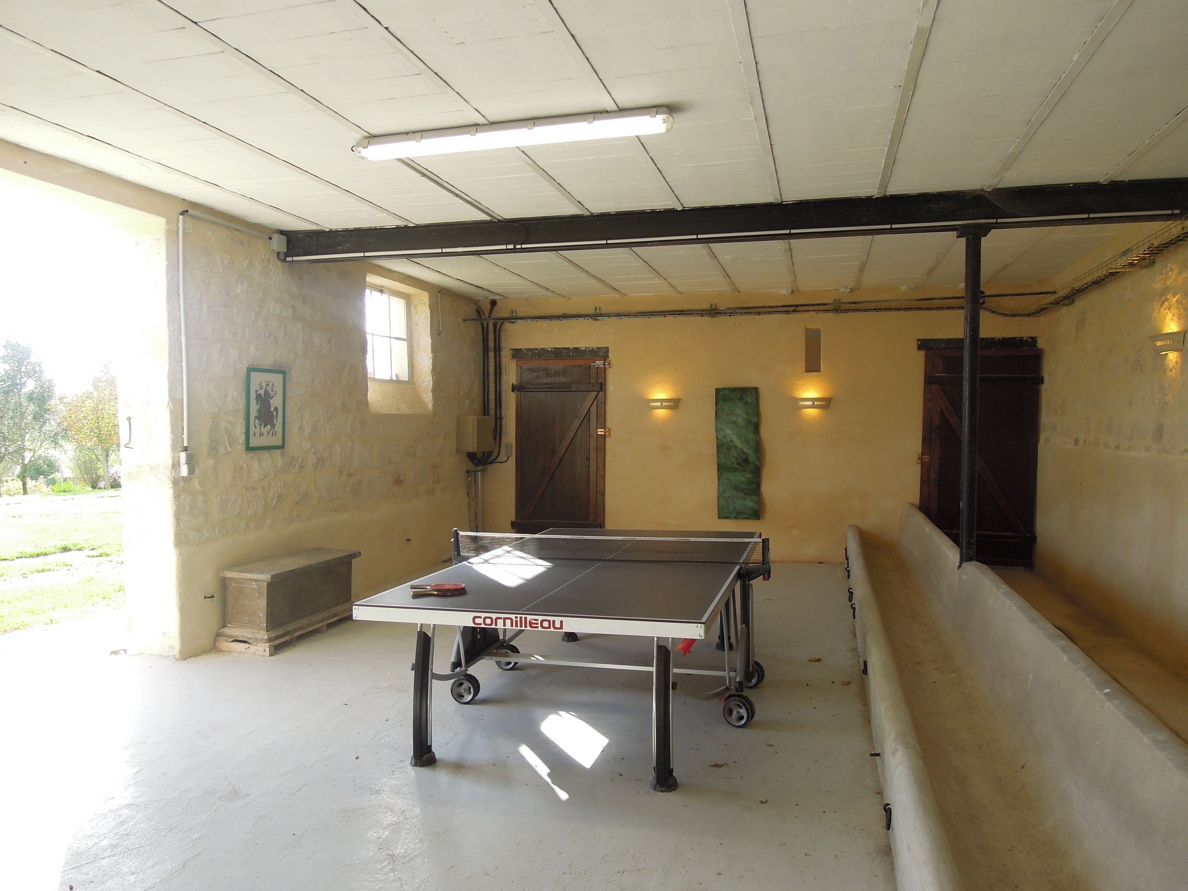 A ping pong table in a room with a ceiling fan, a window, and a wall-mounted light fixture.