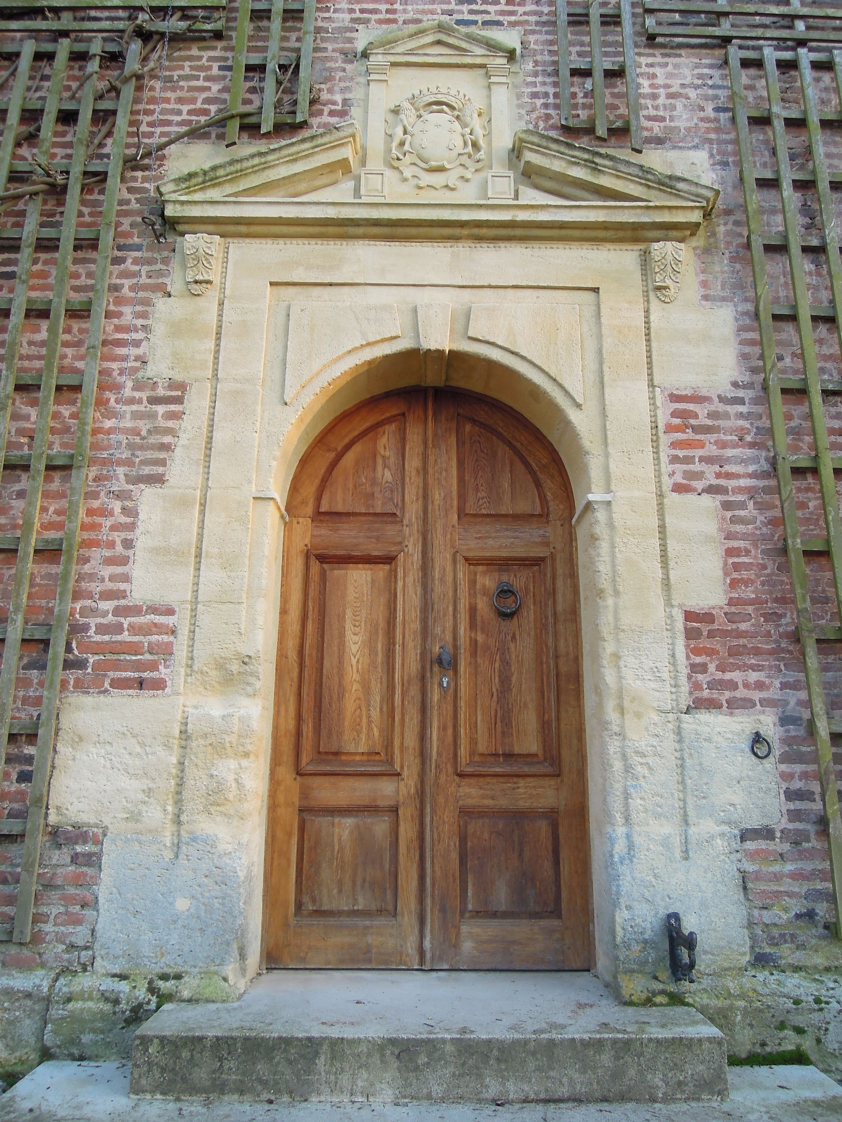 A wooden double door with a stone archway, set in a brick building with a decorative crest above.