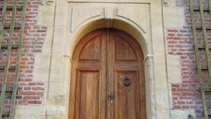 A wooden double door with a stone archway, set in a brick building with a decorative crest above.