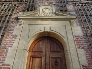 A wooden door with a decorative arch and a coat of arms above it, set in a brick wall.