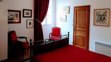 A bedroom with a bed, a red chair, a wooden door, and framed pictures on the walls.