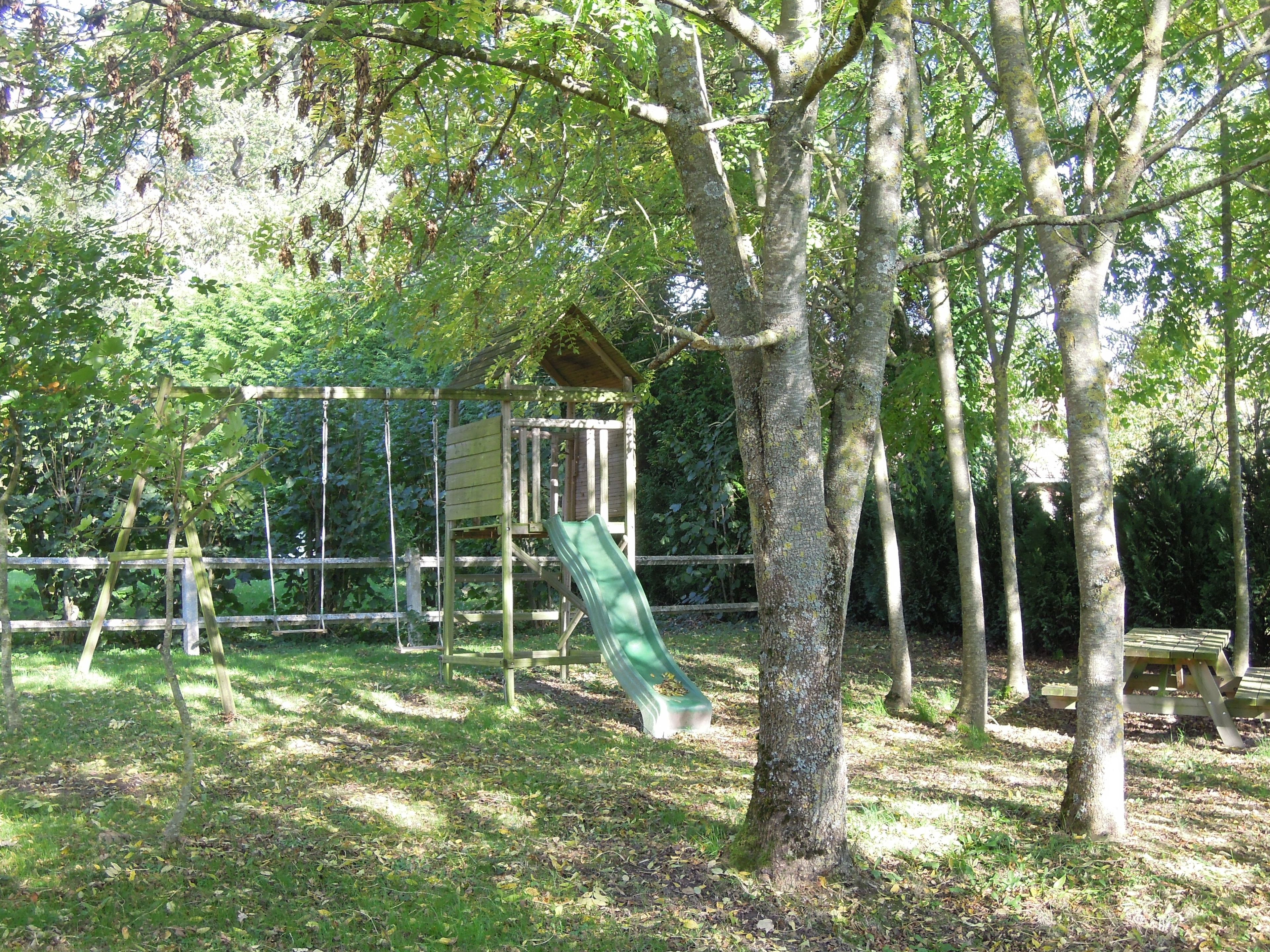 Un parque infantil con tobogán y estructuras para escalar, rodeado de árboles y una mesa de picnic.