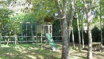 Un parque infantil con tobogán y estructuras para escalar, rodeado de árboles y una mesa de picnic.
