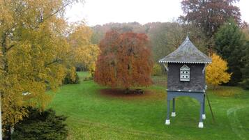 A small, standalone structure with a pointed roof, situated in a grassy area with trees displaying autumn foliage.