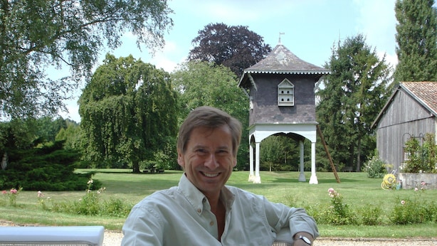 A man seated at an outdoor table with a clear view of a gazebo and a barn in the background.