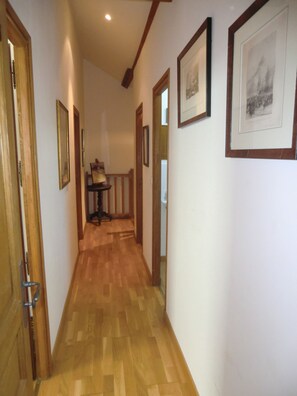 A hallway with wooden flooring, framed pictures on the walls, and a door on the left.
