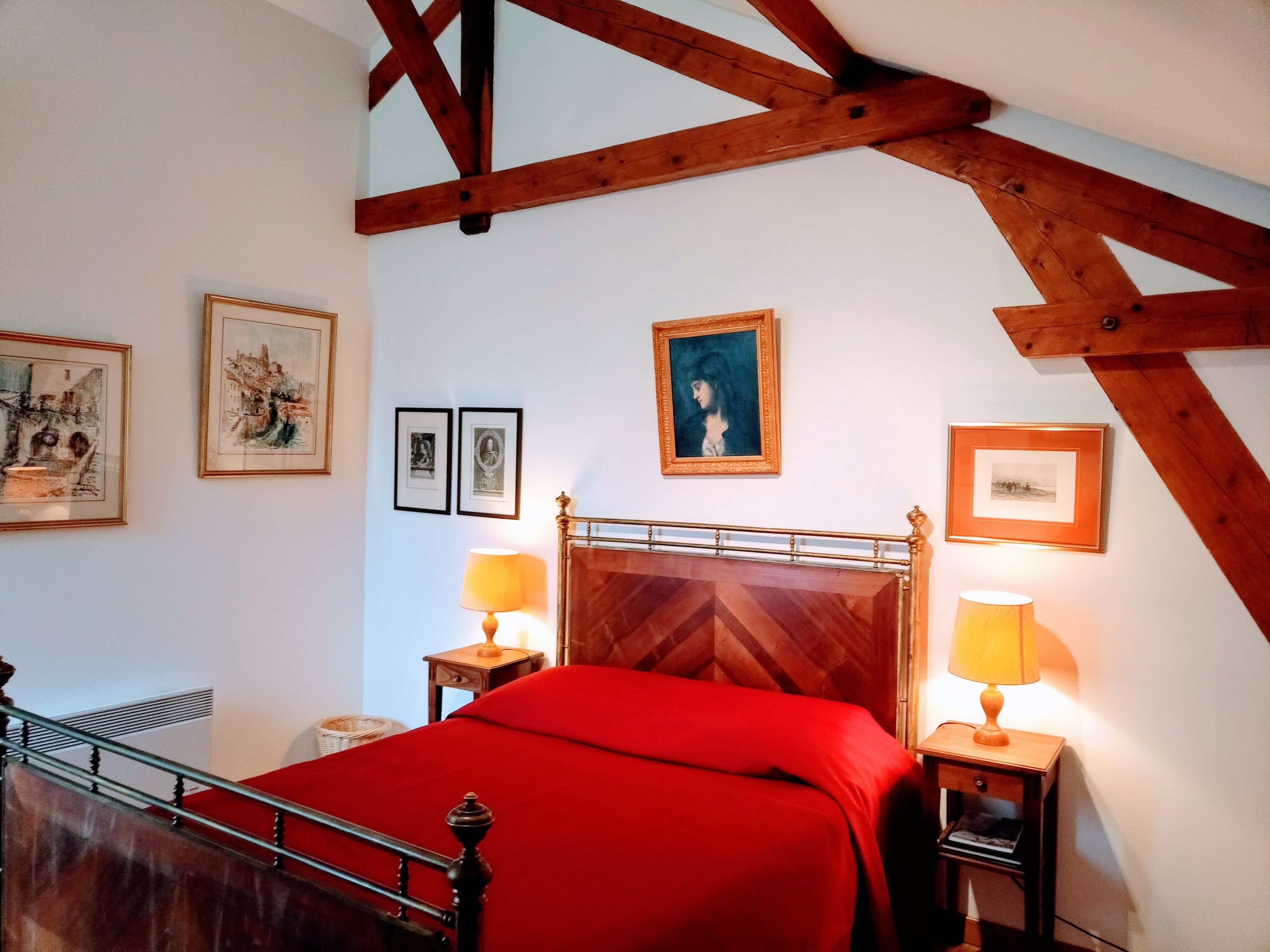 A bedroom with a wooden headboard, a red bedspread, two bedside lamps, and framed artwork on the walls.