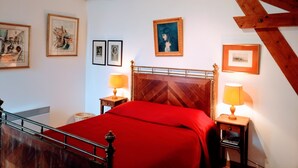 A bedroom with a wooden headboard, a red bedspread, two bedside lamps, and framed artwork on the walls.
