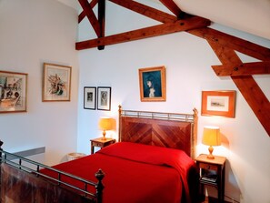 Un dormitorio con cabecera de madera, colcha roja, dos lámparas de noche y cuadros en las paredes.