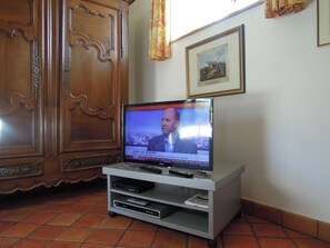 Un téléviseur posé sur un meuble, avec une télécommande, un lecteur DVD et un cadre photo accroché au mur.