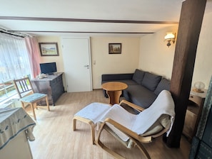 A cozy room with a sofa, two chairs, a small table, a desk with a computer, and a window with curtains.