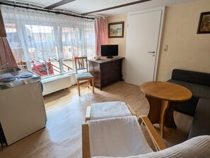 A room with a kitchenette, a wooden dining table, a sofa, a television, and a window with curtains. - Nostalgic Apartment "Hühnerstall" with Unique Charm (Garden Access, Wi-Fi, Parking) (Hörselberg-Hainich)