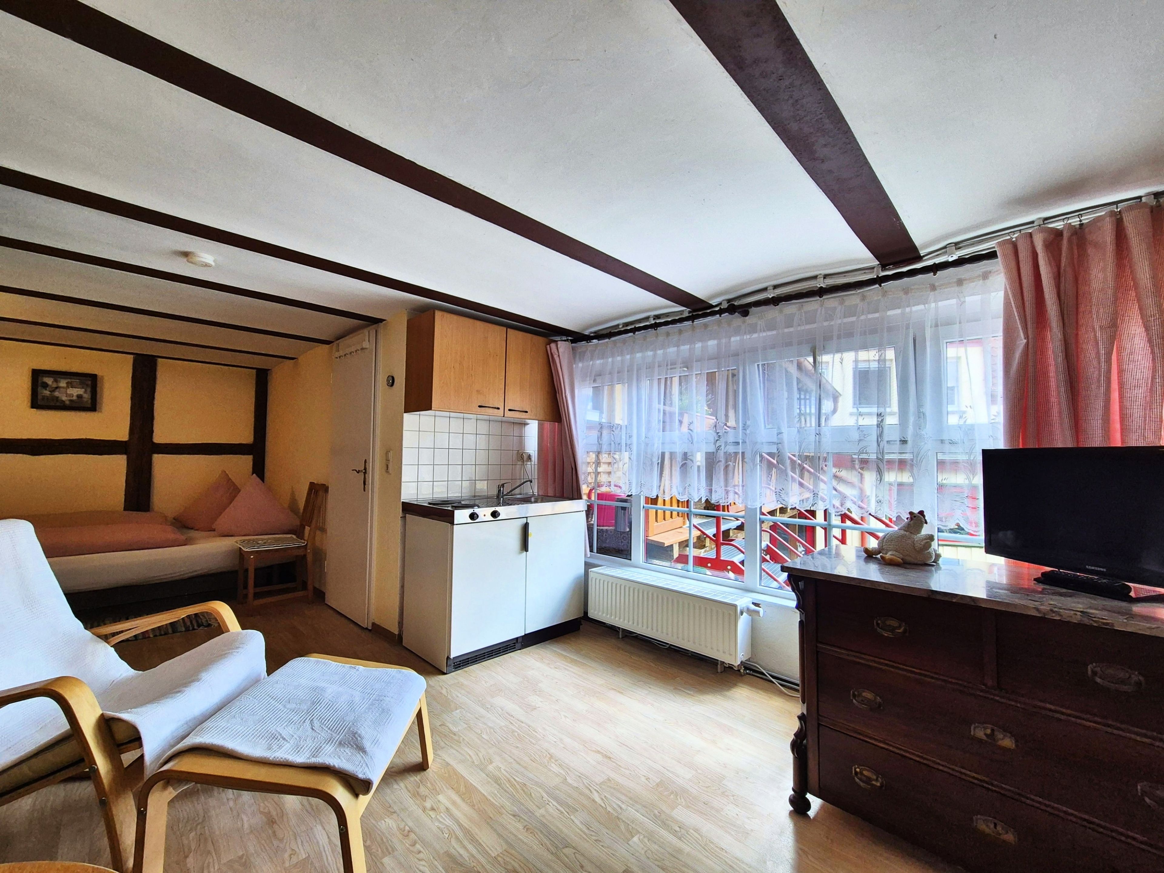 Espacio habitable pequeño con kitchenette, cama, televisor y vista de una escalera roja en el exterior.