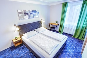 A hotel room with a bed, bedside tables, a desk, and a window with curtains. - Smarthotel Schmid (Sitzenberg)