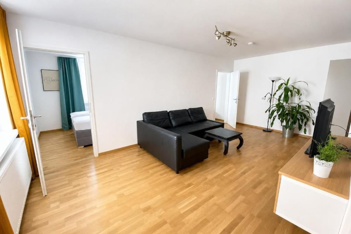 Un salon moderne avec un canapé d’angle, une table basse et un téléviseur posé sur un meuble en bois.