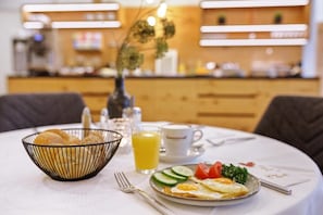 Une table mise pour le petit-déjeuner, avec une assiette d’œufs, des légumes et un verre de jus d’orange.