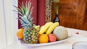 Eine Obstplatte mit Ananas, Bananen, Orangen und einer Melone auf einem weißen Teller.