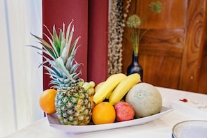 Une assiette blanche garnie d’une variété de fruits : ananas, bananes, oranges et melon.