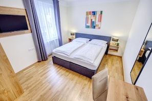 Une chambre d’hôtel avec un lit, des tables de chevet, une télévision et un miroir.