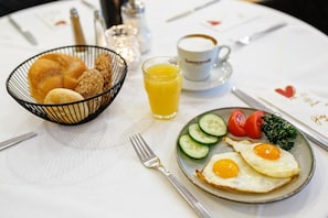 Une table mise pour le petit-déjeuner avec une assiette d’œufs, des légumes et un verre de jus d’orange.