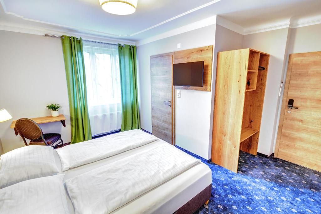 A hotel room with a bed, a desk, a chair, a TV mounted on the wall, and a wardrobe.