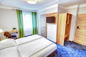 A hotel room with a bed, a desk, a chair, a TV mounted on the wall, and a wardrobe. - Smarthotel Schmid (Sitzenberg-Reidling)
