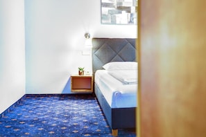 A small, neatly arranged bedroom with a bed, a nightstand with a lamp, and a small plant. - Smarthotel Schmid (Sitzenberg)
