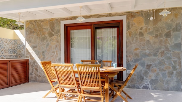 Un patio al aire libre con un muro de piedra, una mesa de madera con sillas y un ventanal de vidrio.
