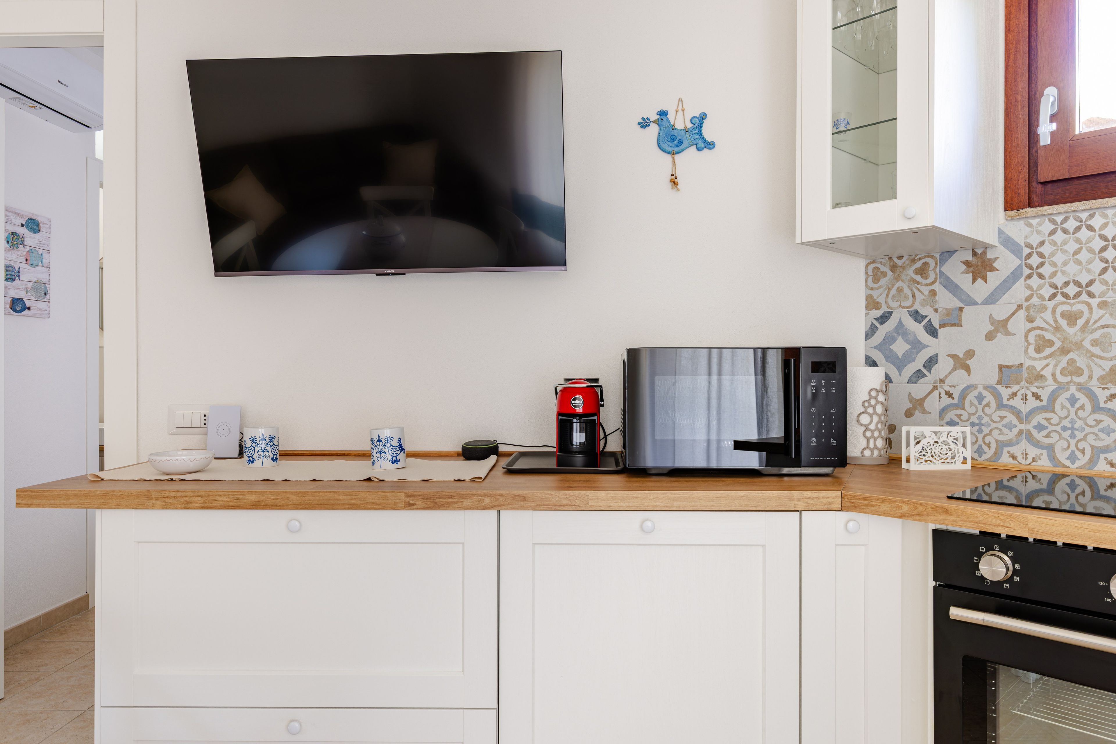 A kitchen with a flat-screen TV mounted above the counter, a coffee maker, a microwave, and a toaster.