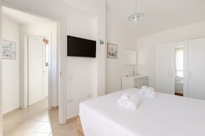 A hotel room with a bed, a TV mounted on the wall, a small desk, and a wardrobe. - Villa Le Pavoncelle Home Holiday – Private Garden, 3 Bedrooms, Near the Beach (Eden Rock)