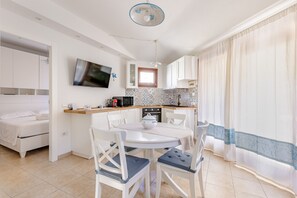 A modern kitchen with a dining area, a TV mounted on the wall, and a window with curtains.