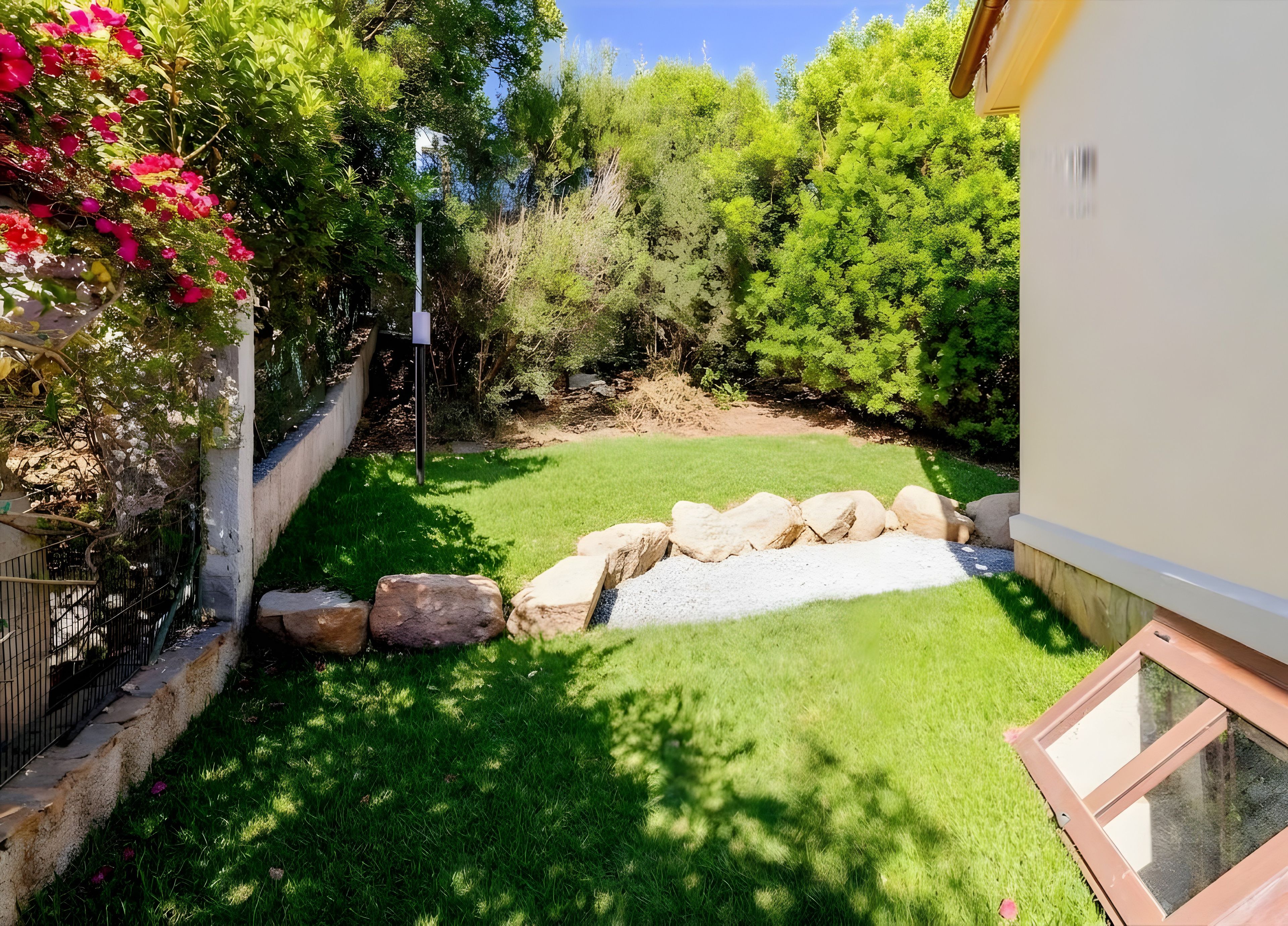 Ein gepflegter Garten mit Rasenfläche, einem kleinen Wasserspiel und einer Steinmauer.